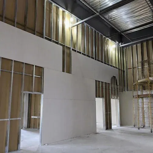 Tall commercial partition walls being boarded from staging, with deck-height framing behind