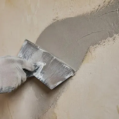 Trowel smoothing fresh plaster over a settlement crack, keyed into the sound material around it