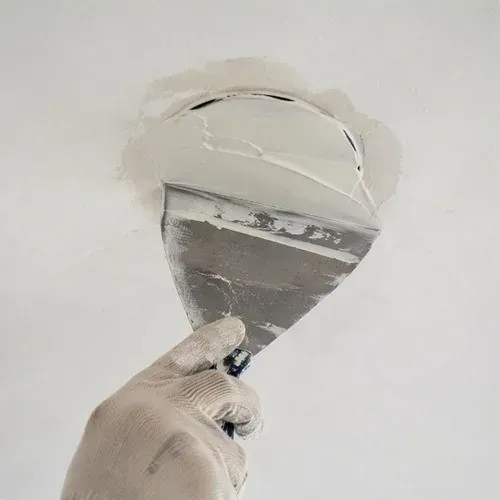 Mudding over patched recessed light holes, feathered wide across the ceiling