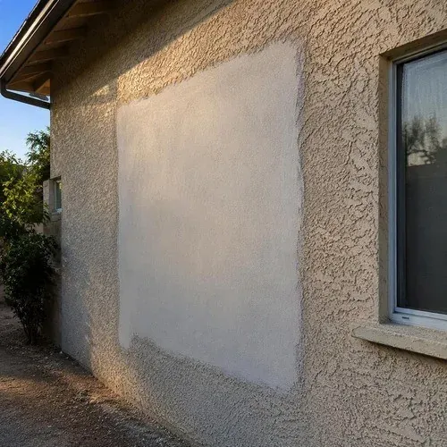 Stucco patch curing against the older textured wall while the texture match is worked in