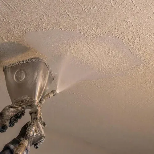 Spraying texture onto a repaired ceiling, dialled in on a test board first to match the original