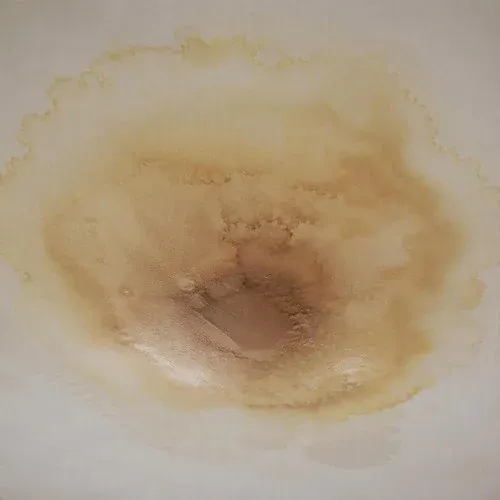 Brown water stain spreading across bedroom ceiling drywall from a leak above