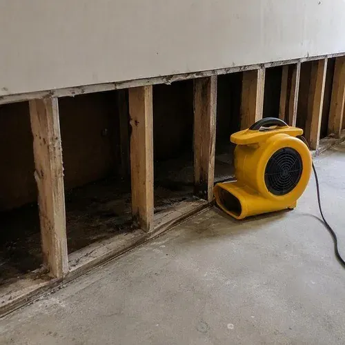 Fan drying an opened wall cavity after a basement flood, before any new board goes on